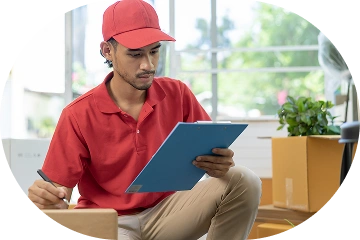 Un livreur assis parmi des cartons de déménagement et vérifiant une liste d'inventaire, représentant des services professionnels de déménagement et de logistique.