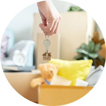 Une main tenant les clés d'une maison au-dessus d'un carton de déménagement, symbolisant le déménagement, l'accession à la propriété et le jour du déménagement.