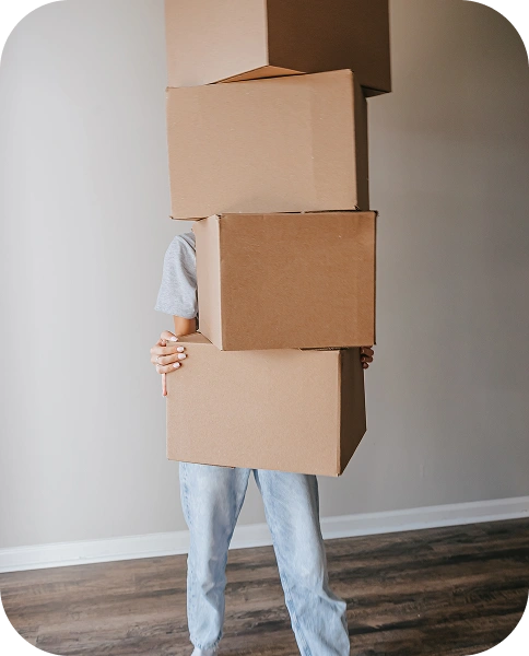 Personne transportant des cartons empilés à l'intérieur, illustrant le processus de déménagement, d'emballage et de transport.